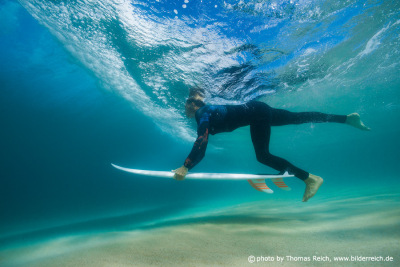 Surfer with surf board duck diving underwater under ocean reflected surface