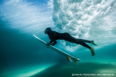Young surfer dives under the ocean wave with surfboard