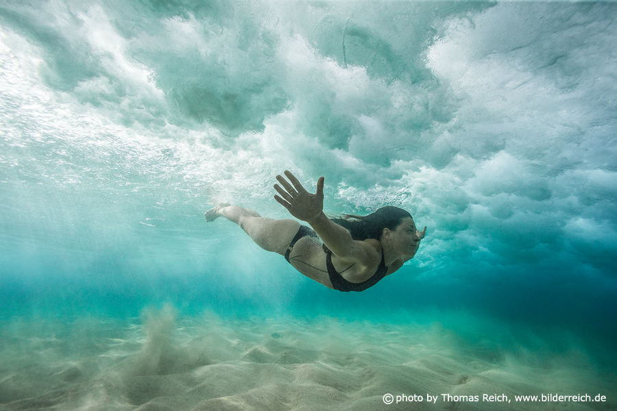 Frau im Bikini taucht unter Welle