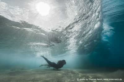 Woman swims with ocean wave and sun rays under water