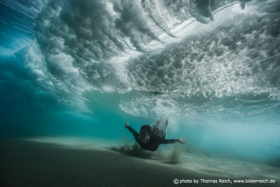 Woman in neoprene dives under a wave