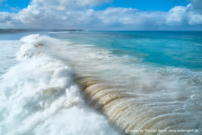 Große Welle bricht am Strand mit Sand