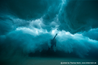 Women diving below huge breaking wave