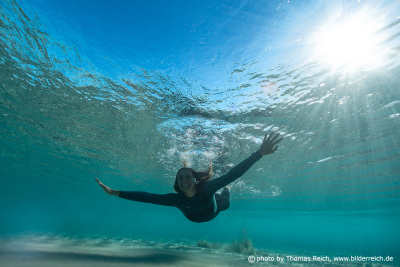 Frau schwimmt unter Wasser mit schönen Sonnenstrahlen