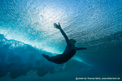 Female Surfer plunge beneath ocean wave