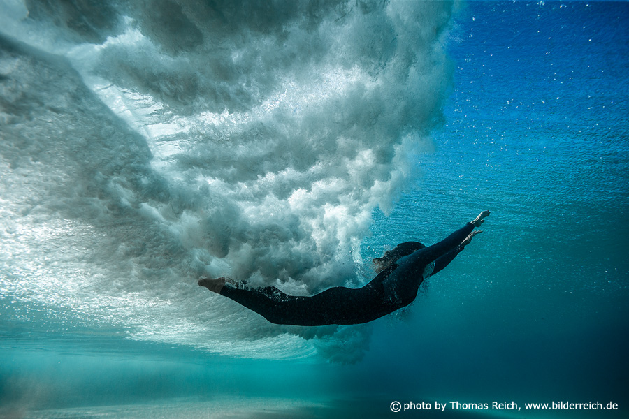 Frau taucht mit Ozeanwelle unter Wasser